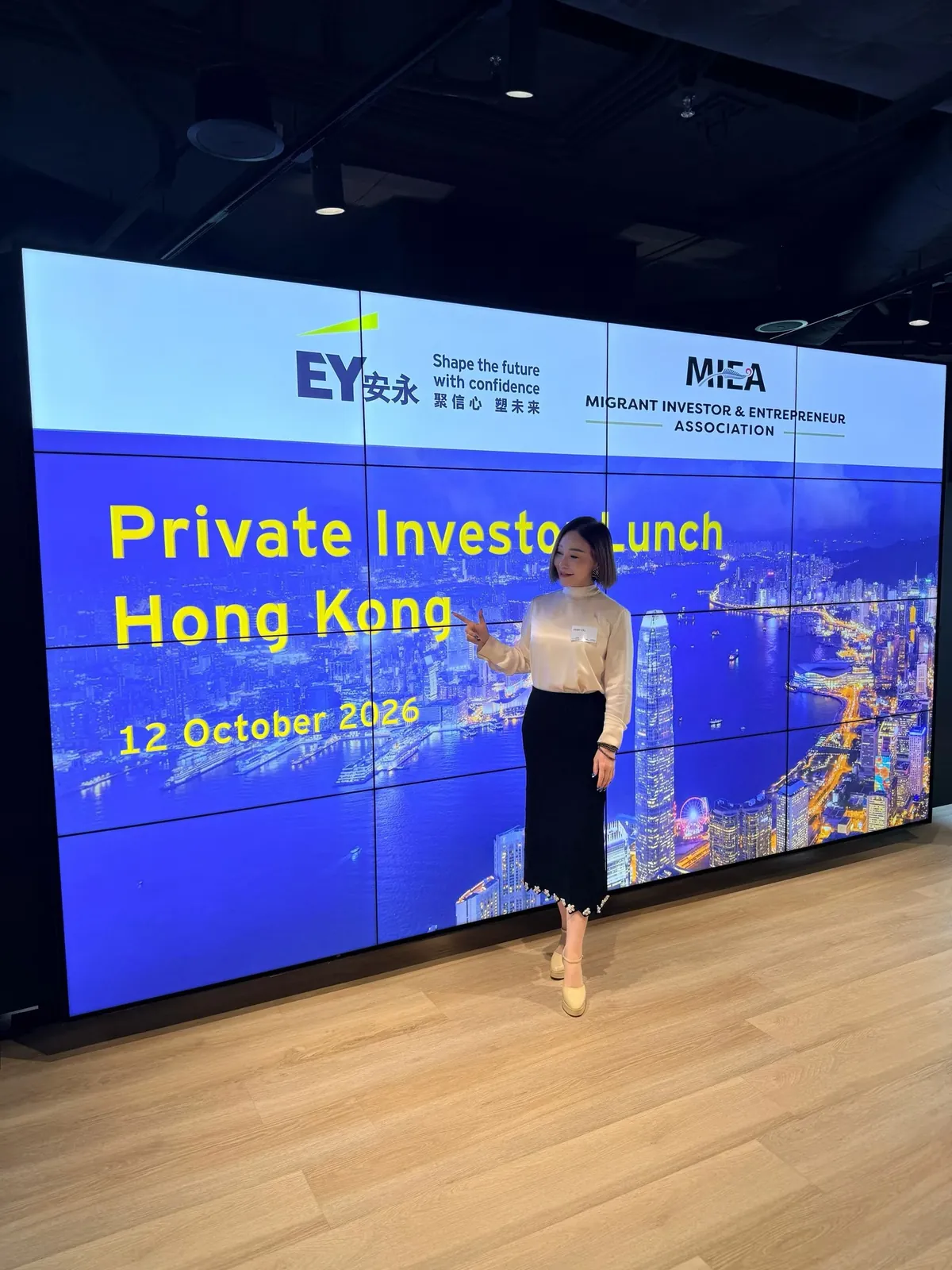 胡静站在香港 MIEA Private Investor Lunch 活动大屏前